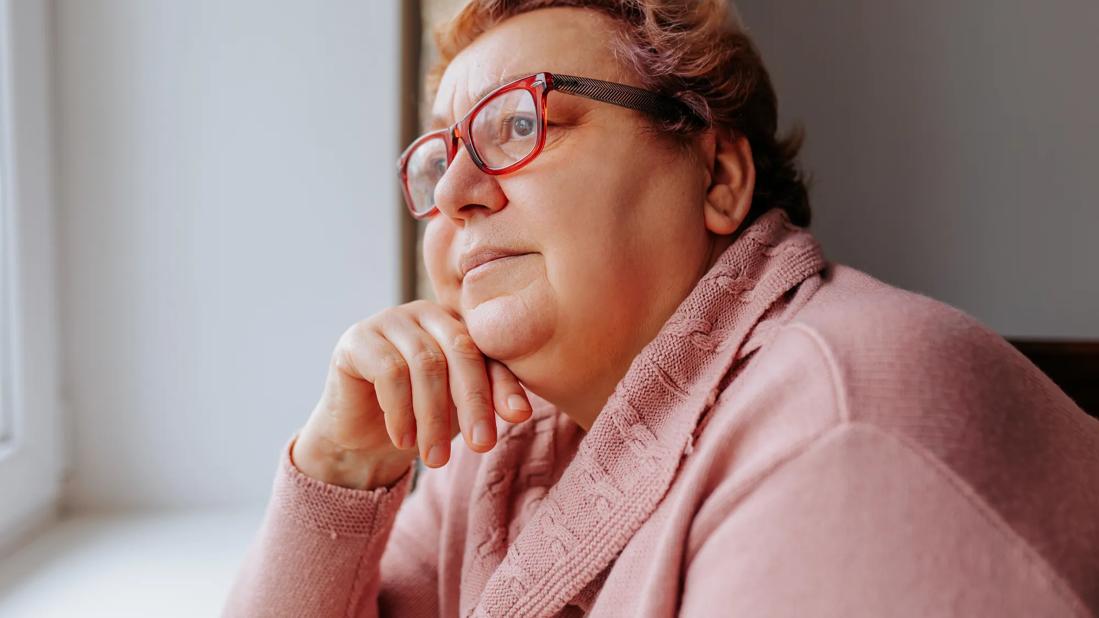 A woman seated by a window, lost in thought, with a contemplative expression, symbolizing the potential benefits of GLP-1 agonists in lowering the risk of age-related macular degeneration
